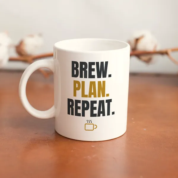 White 11 oz ceramic mug printed with "Brew. Plan. Repeat." on a wooden table