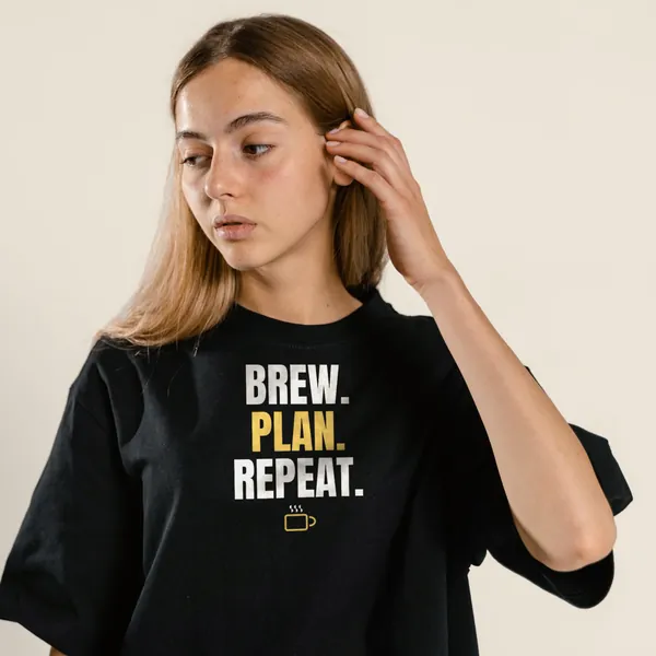 Model wearing a black "Brew. Plan. Repeat." tee with the light-ink version of the design