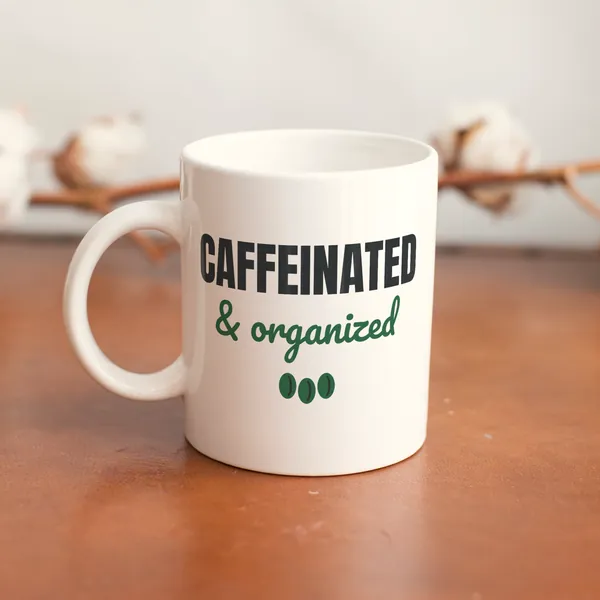 White 11 oz ceramic mug printed with "Caffeinated and Organized" on a wooden table