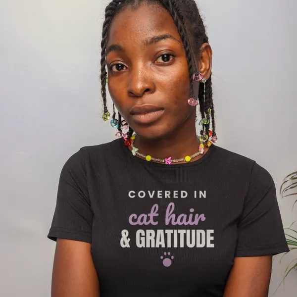 Woman wearing a black "Covered in Cat Hair and Gratitude" tee in a studio (light-ink print for dark shirts)