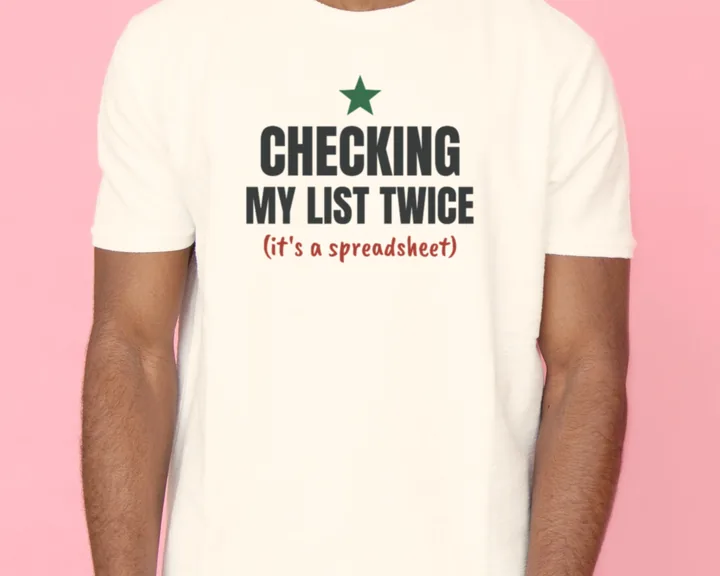Man wearing a white "Checking My List Twice (It's a Spreadsheet)" tee against a pink backdrop
