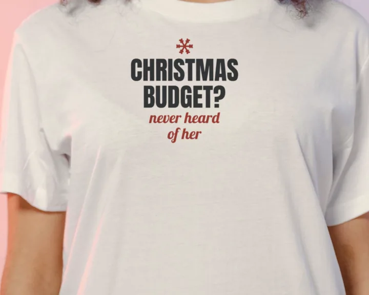 Woman wearing a white "Christmas Budget? Never Heard of Her" tee against a soft pastel backdrop