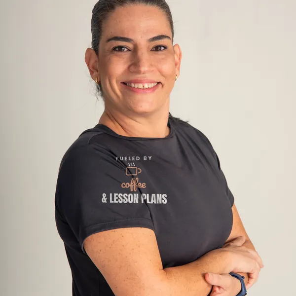 Woman wearing a black "Fueled by Coffee and Lesson Plans" tee in a bright studio (light-ink print for dark shirts)