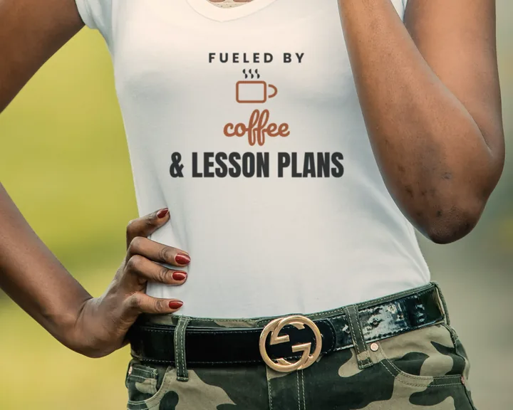 Woman wearing a white "Fueled by Coffee and Lesson Plans" tee outdoors in a park