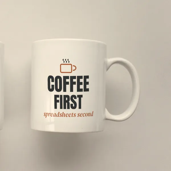 White 11 oz ceramic mug printed with "Coffee First, Spreadsheets Second", side view
