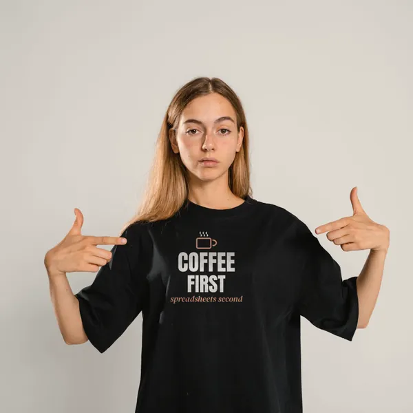 Woman wearing a black "Coffee First, Spreadsheets Second" tee in a studio (light-ink print for dark shirts)