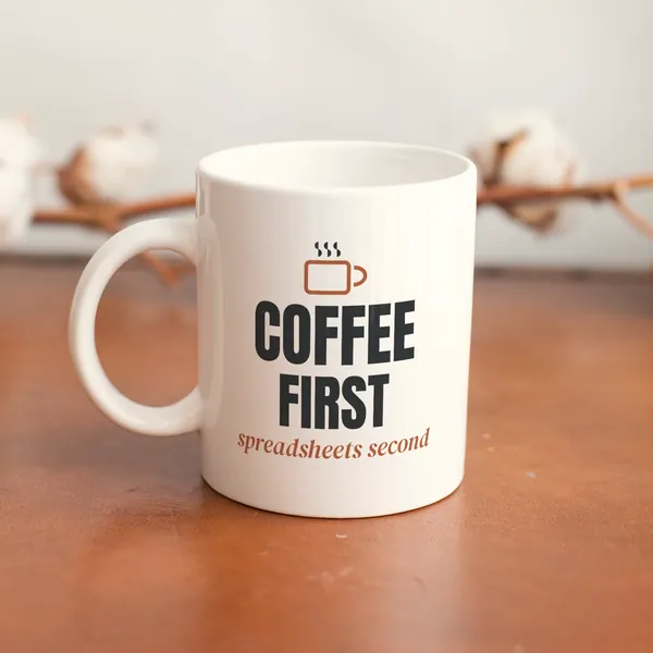 White 11 oz ceramic mug printed with "Coffee First, Spreadsheets Second" on a wooden table