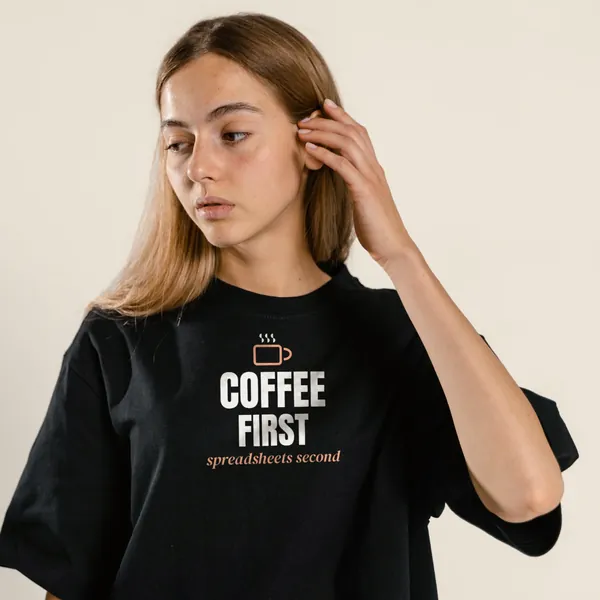 Model wearing a black "Coffee First, Spreadsheets Second" tee with the light-ink version of the design