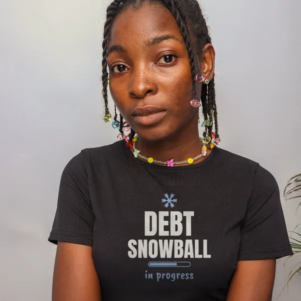 Woman wearing a black "Debt Snowball in Progress" tee in a studio (light-ink print for dark shirts)