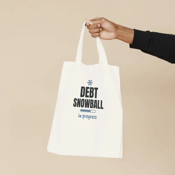 Natural canvas tote bag printed with "Debt Snowball in Progress", held by the handles