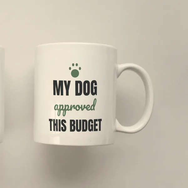 White 11 oz ceramic mug printed with "My Dog Approved This Budget", side view