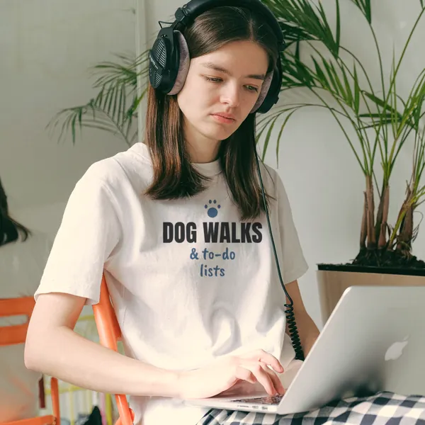 Woman wearing a white "Dog Walks and To-Do Lists" tee working on a laptop in a home office