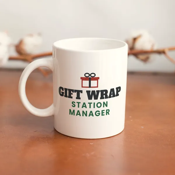 White 11 oz ceramic mug printed with "Gift Wrap Station Manager" on a wooden table