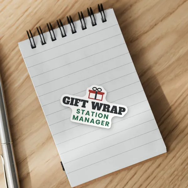 Die-cut "Gift Wrap Station Manager" vinyl sticker on a spiral notepad