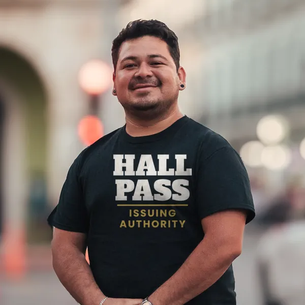 Man wearing a black "Hall Pass Issuing Authority" tee outdoors on a city street (light-ink print for dark shirts)