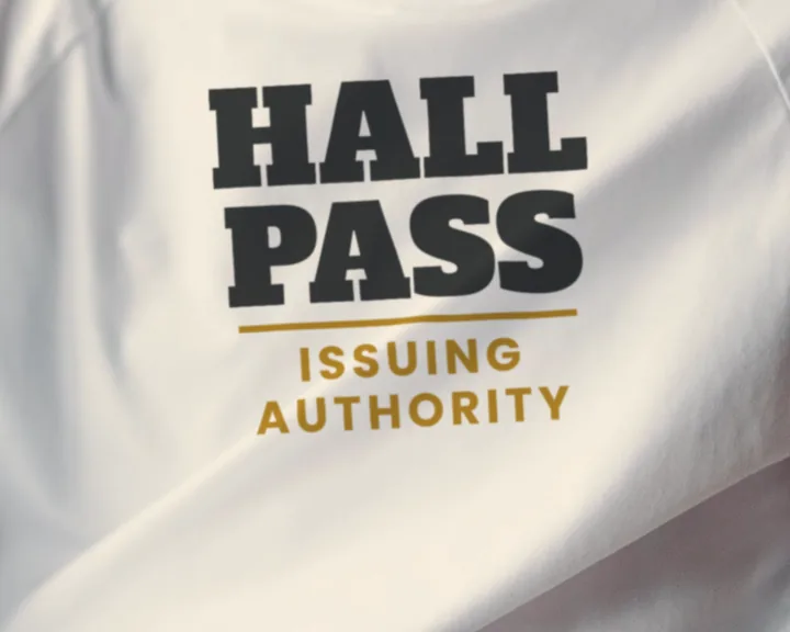 Man wearing a white "Hall Pass Issuing Authority" tee at home by a green wall