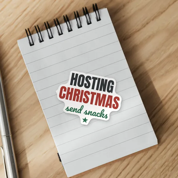 Die-cut "Hosting Christmas, Send Snacks" vinyl sticker on a spiral notepad