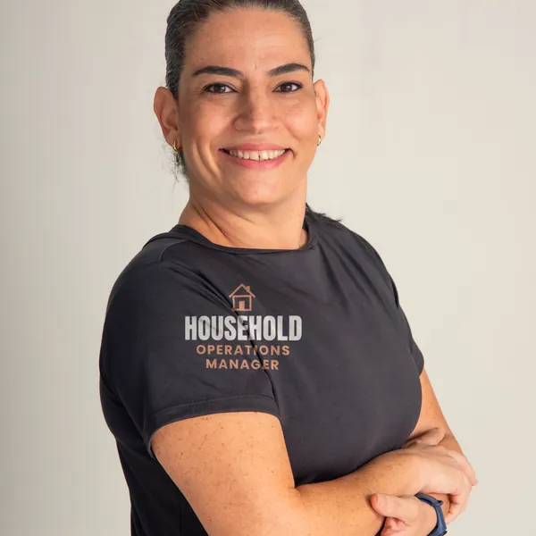 Woman wearing a black "Household Operations Manager" tee in a bright studio (light-ink print for dark shirts)