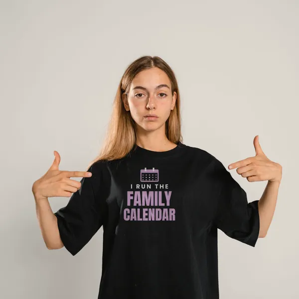 Woman wearing a black "I Run the Family Calendar" tee in a studio (light-ink print for dark shirts)