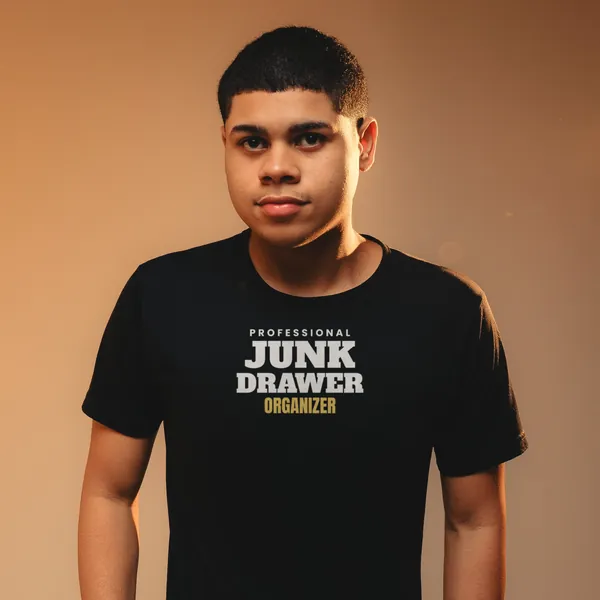 Man wearing a black "Professional Junk Drawer Organizer" tee against a warm backdrop (light-ink print for dark shirts)