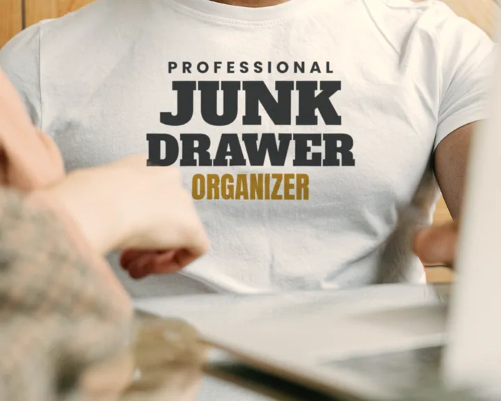 Man wearing a white "Professional Junk Drawer Organizer" tee in an office with a wooden wall