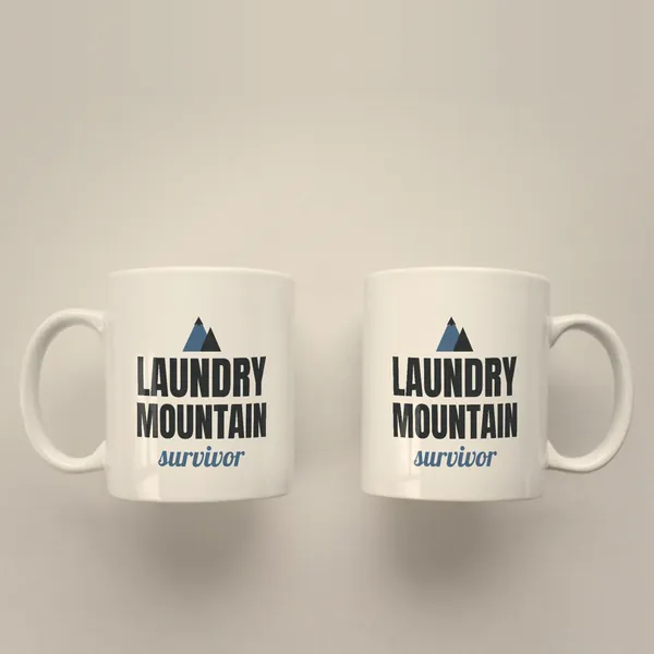 Two white 11 oz ceramic mugs printed with "Laundry Mountain Survivor", handles left and right