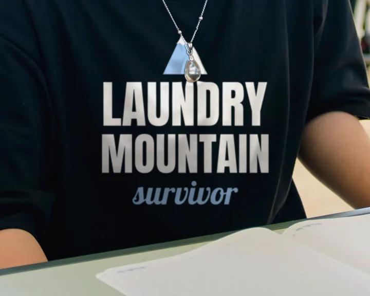 Woman wearing a black "Laundry Mountain Survivor" tee at a desk in a computer lab (light-ink print for dark shirts)