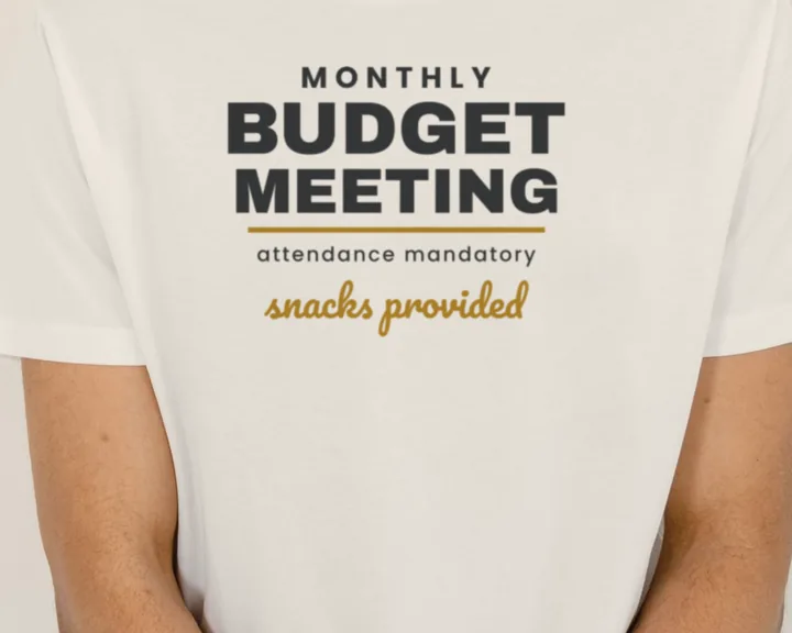 Man wearing a white "Monthly Budget Meeting - Snacks Provided" tee in a bright studio