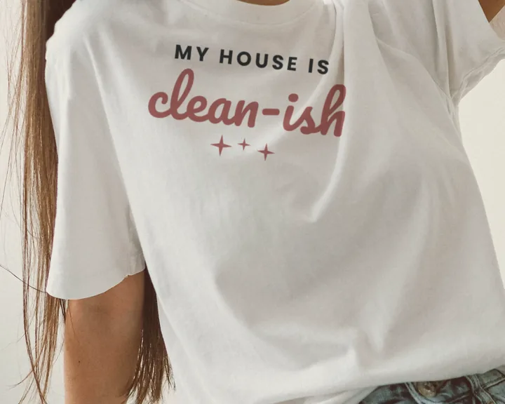 Woman wearing a white "My House Is Clean-ish" tee relaxing at home