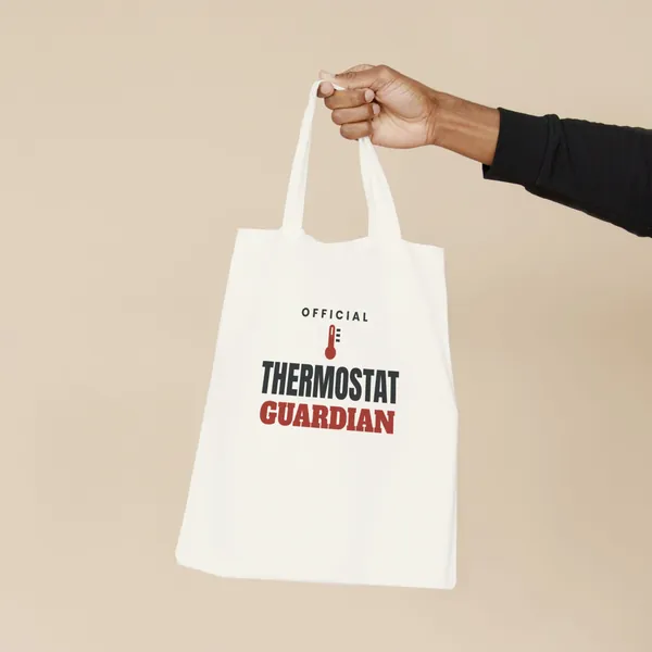 Natural canvas tote bag printed with "Official Thermostat Guardian", held by the handles