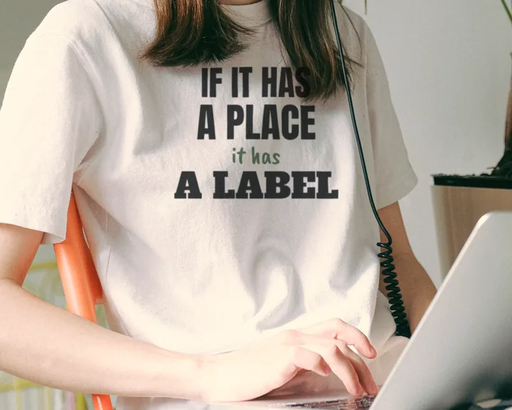 Woman wearing a white "If It Has a Place, It Has a Label" tee working on a laptop in a home office