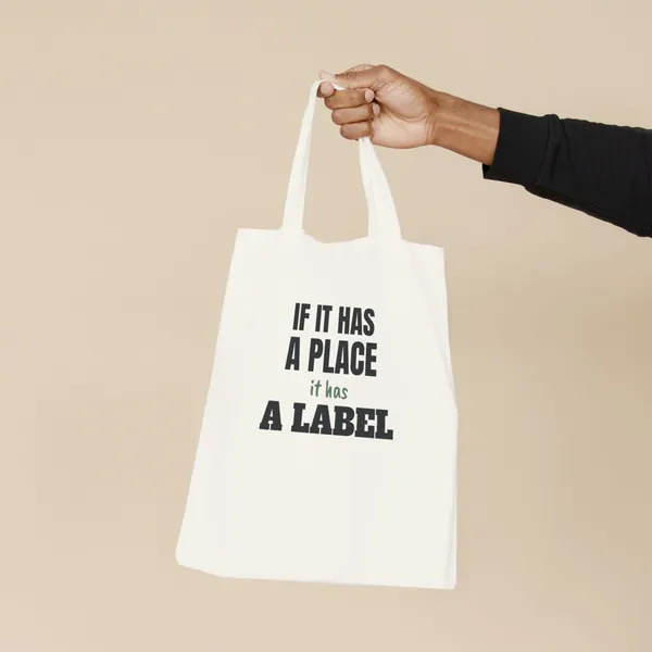 Natural canvas tote bag printed with "If It Has a Place, It Has a Label", held by the handles
