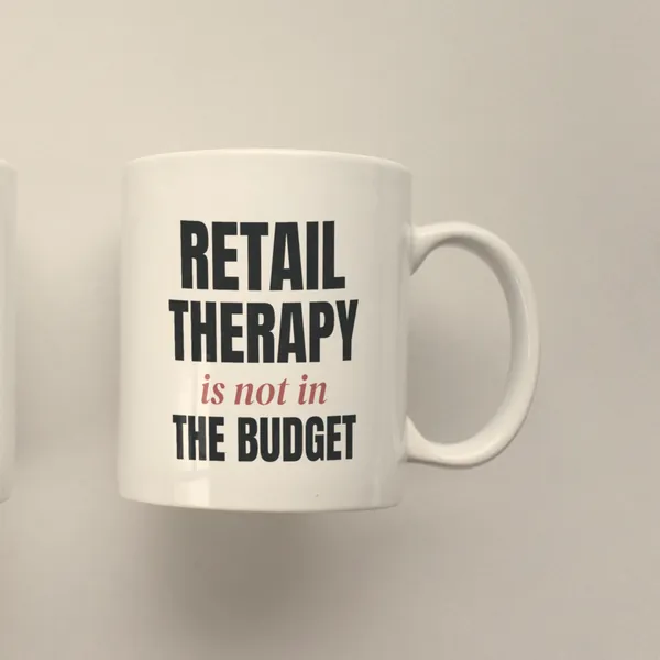 White 11 oz ceramic mug printed with "Retail Therapy Is Not in the Budget", side view