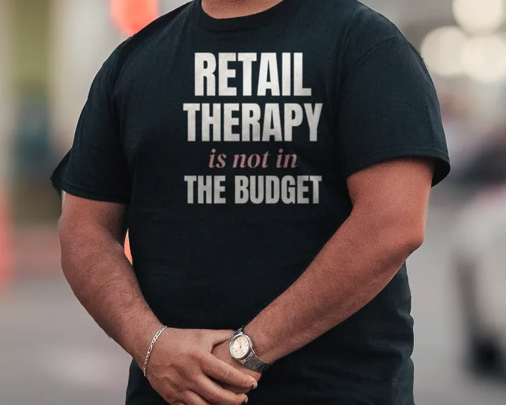Man wearing a black "Retail Therapy Is Not in the Budget" tee outdoors on a city street (light-ink print for dark shirts)