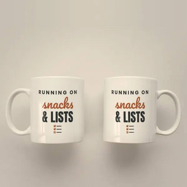 Two white 11 oz ceramic mugs printed with "Running on Snacks and Lists", handles left and right