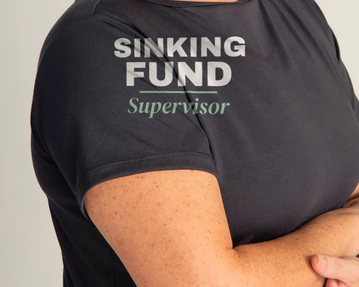 Woman wearing a black "Sinking Fund Supervisor" tee in a bright studio (light-ink print for dark shirts)