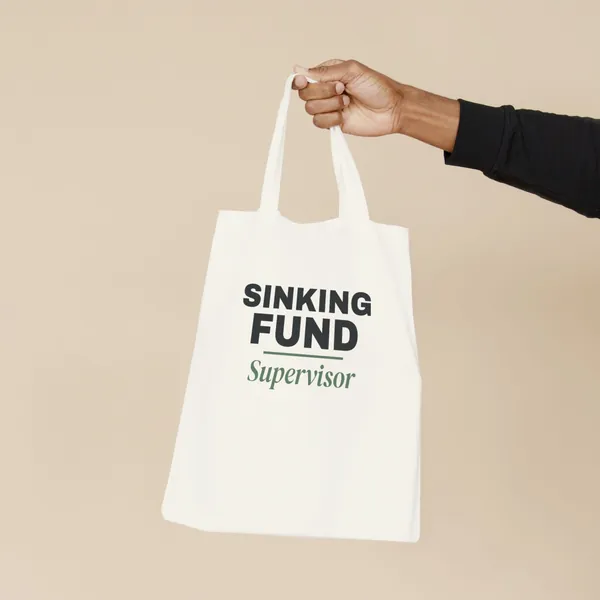 Natural canvas tote bag printed with "Sinking Fund Supervisor", held by the handles