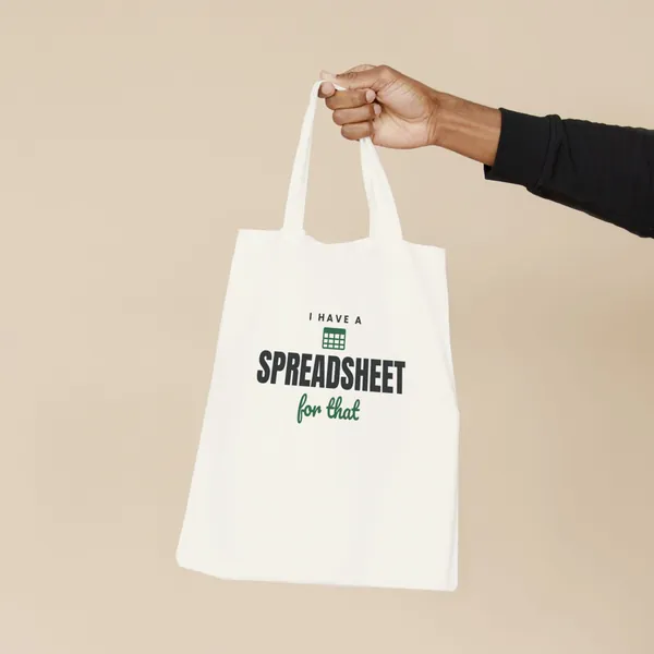 Natural canvas tote bag printed with "I Have a Spreadsheet for That", held by the handles